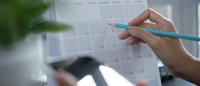 Planification de rendez-vous avec Daniel Bousquet à Toulouse, main pointant une date sur calendrier, smartphone à la main,